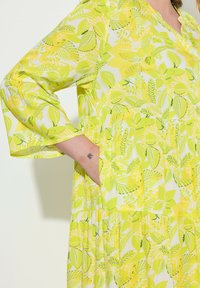 Sukienka w kwiatowy wzór w jasnych odcieniach żółci i zieleni, o luźnym kroju, z rękawami do połowy przedramienia i kieszeniami po bokach. Lekka tkanina.