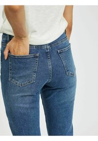 Jeans de ganga azuis com um design justo, apresentando dois bolsos traseiros e uma cintura média. A textura é suave e ligeiramente elástica.