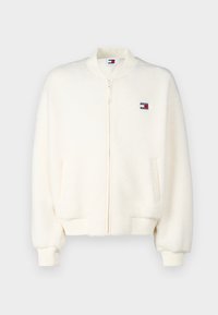 Chaqueta bomber de forro polar en color crema con puños y dobladillo acanalados, cremallera completa y parche de logo en el pecho. Cuenta con bolsillos laterales.