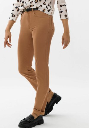 Brown skinny trousers with a smooth texture, featuring front pockets, and paired with black loafers. The outfit is completed by a leopard print top.