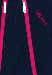 Chaqueta azul marino con cremalleras y costuras rosas. Presenta un logo bordado en rosa. El material parece suave y duradero.