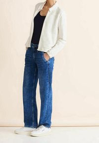 Biała teksturowana kurtka, granatowa bluzka, niebieskie proste dżinsy, białe trampki. Kurtka ma kołnierz i zamek błyskawiczny; dżinsy mają przednie kieszenie.