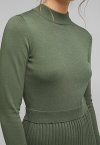 Groen geribbeld gebreid sweater met een hoge hals, lange mouwen en een aansluitende taille. Soepele textuur met subtiele verticale lijnen.