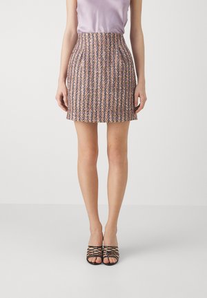 Jupe courte ajustée en tissu tweed multicolore avec des rayures verticales. Associée à un haut sans manches violet clair et des sandales à talons noirs.