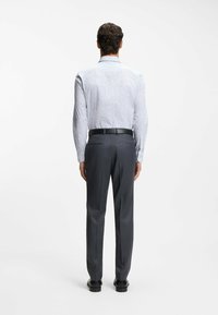 Langärmeliges Hemd in Hellblau mit kleinen dunklen Punkten, kombiniert mit dunkelgrauen Hosen. Das Outfit wird durch einen schwarzen Gürtel und elegante Schuhe ergänzt.