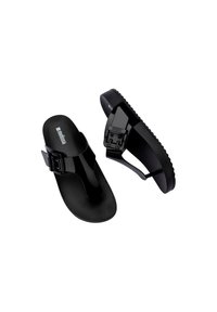 Chanclas negras hechas de material brillante que cuentan con una hebilla ajustable, una suela texturizada y un diseño minimalista con tira entre los dedos.