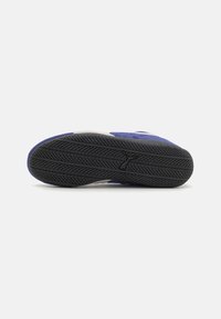 Blå sneakers med grå detaljer, med en teksturert gummisåle og et mønstrete dekk for grep. Overmaterialet er myk semsket skinn.
