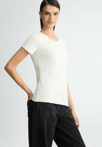 Witte korte mouwen top met een ronde halslijn, voorzien van een gladde textuur en subtiele versieringen bij de halslijn, gecombineerd met zwarte denim jeans.