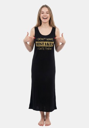 Lächelnde barfüßige Frau in einem langen schwarzen ärmellosen Kleid, die auf goldenen Text zeigt, der lautet "I don't make mistakes I date them."