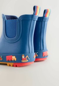 Blauwe rubberen regenlaarzen met een gestructureerd oppervlak en een rode basis. Voorzien van kleurrijke voertuigmotieven en een gestreepte stoffen trekhaak.