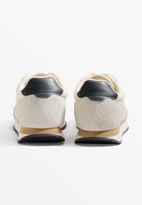 Sneakers med ovandel i vitt läder, grå mockaaccenter och svart läder på hälen. Har en ljusbrun gummisula och texturerade detaljer.