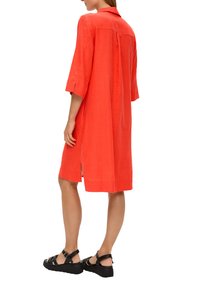 Rotes Leinenkleid mit Kragen, drei Viertelärmeln, seitlichen Schlitzen und lockerer Passform. Kombiniert mit schwarzen Riemchensandalen für den Kontrast.