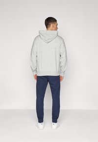 Sivi hoodie s vezicom i kengurujem džepom, u kombinaciji s tamnoplavim trenerkama i bijelim tenisicama, prikazan s leđa.