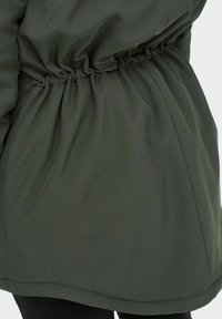 Olivgrön jacka med elastisk midja, tillverkad av slät tyg. Har en rak nederkant och subtil lyster. Ingen hårdvara eller mönster synliga.