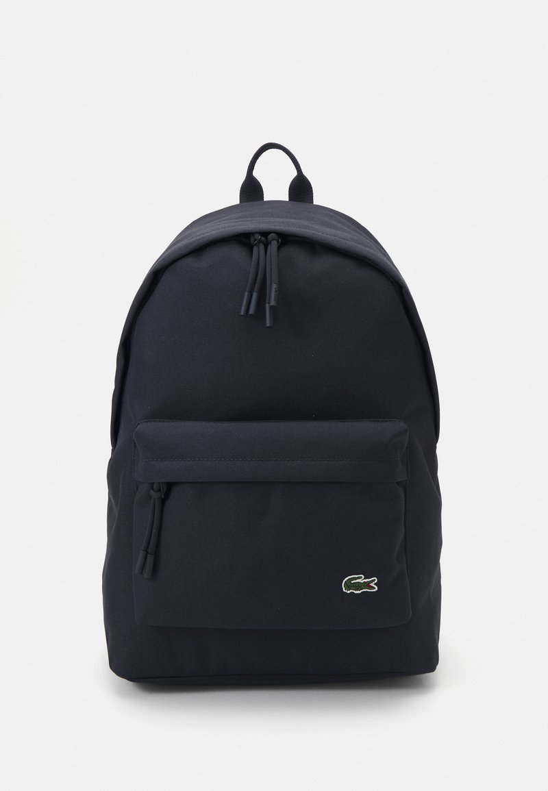 Mochila de lona azul marino con una forma redondeada, asa superior, correas ajustables y un bolsillo frontal con un pequeño logo. Textura suave.