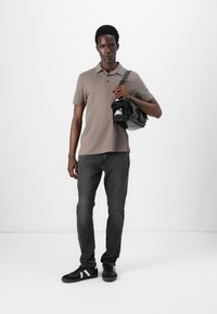 Camisa polo de manga corta en color topo, jeans grises, zapatillas negras y un bolso de hombro de cuero negro. Diseño simple con detalles sutiles.