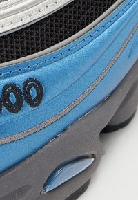 Niebiesko-srebrny sportowy but z teksturowaną siateczką, gładkimi syntetycznymi elementami, amortyzującą podeszwą oraz czarnymi detalami po boku.