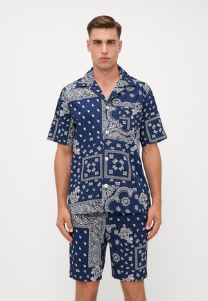 Ensemble comprenant une chemise à manches courtes bleu marine et un short, présentant des motifs paisley et géométriques blancs contrastants, avec un devant boutonné et un col.