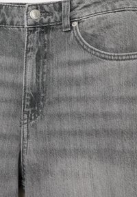 Prim-plan al brâului de blugi gri din denim, cu buton metalic, buclă pentru curea și cusătură la buzunarul din față.