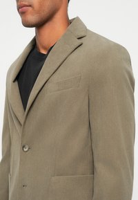 Olijfgroen corduroy blazer met geklauwde zakken, enkele knoopsluiting, borstzak en textuurdetails. Classic tailored silhouet.
