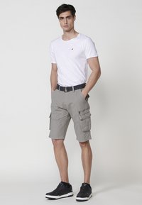 Shorts cargo gris avec plusieurs poches, portés avec un t-shirt blanc à col rond. Une ceinture noire et des baskets noires complètent la tenue.