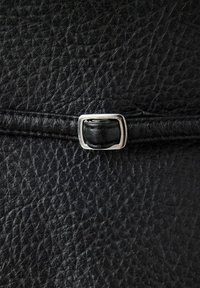 Gros plan sur un cuir noir texturé avec une petite boucle rectangulaire argentée fixée à une fine lanière en cuir.