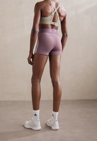 Sport-bh i beige med korsryggdesign, kombinerad med mauve shorts med vita ränder. Vita sportskor och strumpor fulländar looken.