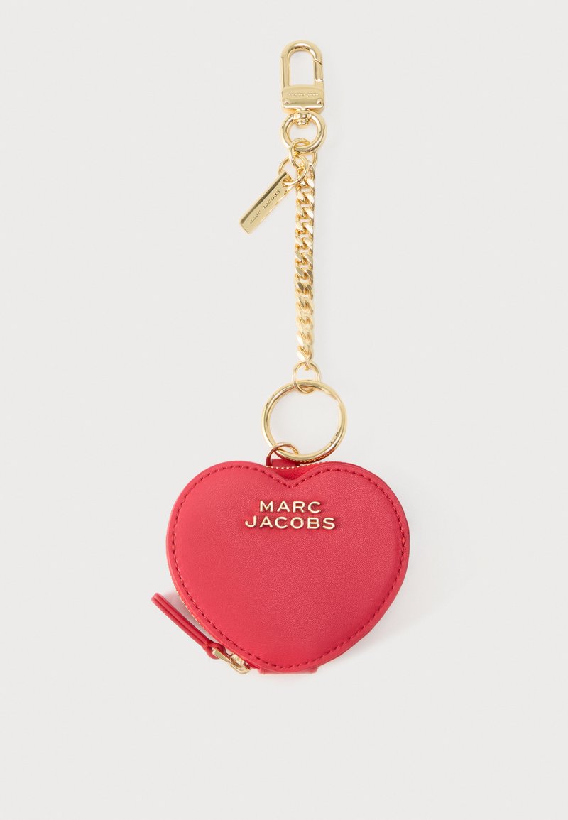 Κόκκινη δερμάτινη θήκη κλειδιών σε σχήμα καρδιάς με χρυστό φερμουάρ, χρυσή αλυσίδα και κούμπωμα, με την επωνυμία "MARC JACOBS" με χρυσά γράμματα.