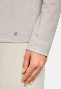 Hellgrauer, gerippter Pullover mit subtilen Glanz, ausgestattet mit einem silbernen Logo-Buttons detail am Saum und einem enganliegenden Bündchen-Design.