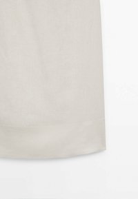 Tissu beige clair avec un simple détail de couture horizontale près du bord inférieur, sur fond blanc.