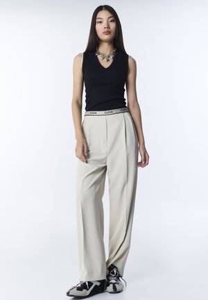 Top nero senza maniche con scollo a V, abbinato a pantaloni a vita alta color crema con cintura decorativa e sneakers nere e grigie.