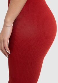 Rote gerippte Leggings aus dehnbarem Material, mit schmaler Passform und glatter Textur sowie subtilen Details entlang der Nähte.