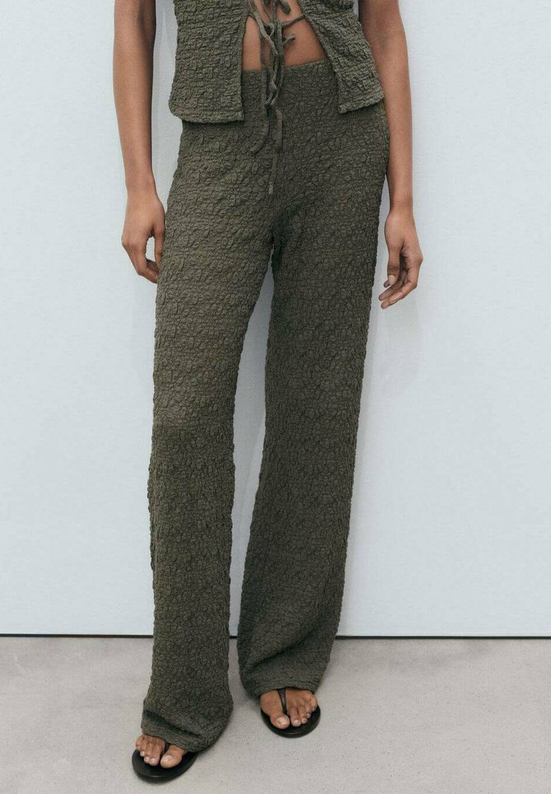 Olivovo zelený cropped top a široké nohavice z textúrovaného materiálu. Voľný strih so šnúrkou v páse. Čierne sandále na otvorenej špičke.