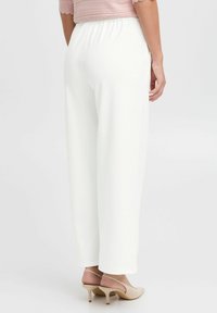 White, wide-leg pants with an elastic waistband, made from smooth fabric. The model wears beige heels, showing a relaxed fit and drape.
