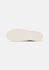 Sole di sneaker bianca in gomma con un motivo testurizzato, caratterizzata da un logo al centro. Il design include forme circolari e a X.