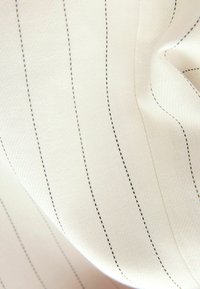 Tissu crème clair avec des rayures noires verticales, présentant une texture lisse et un léger éclat, mettant en avant un détail de tissage fin.