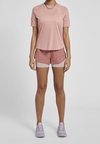 Camiseta deportiva de manga corta en rosa claro combinada con pantalones cortos rosas con detalles en beige, modelo lleva zapatillas deportivas lavanda.