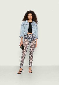 Casaco de ganga sobre uma top cropped preta, combinado com leggings justas com um padrão de borboletas em tons de cinza e creme. Clutch preta e saltos altos.