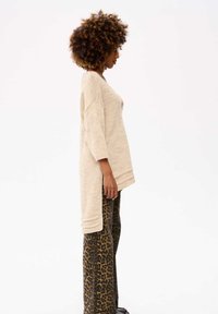 Beige gebreide trui met losse pasvorm en driekwartmouwen, gecombineerd met brede broek met luipaardprint. Zachte textuur en ontspannen ontwerp.