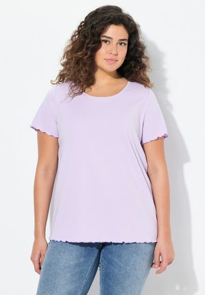 T-shirt corto a maniche corte di un leggero colore viola, con bordi ondulati, scollo rotondo e vestibilità rilassata, abbinato a jeans azzurri chiari.