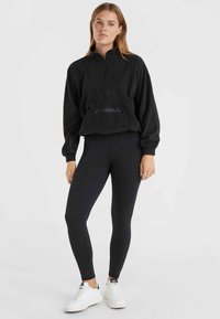 Pull en polaire noir à fermeture éclair quart sur le devant, associé à un legging noir et des baskets blanches. Poignets et taille élastiques.