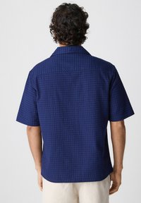 Marineblauw kortarm shirt met een gestructureerd patroon, een kraag en een rechte zoom. De achterkant toont de details en de structuur van de stof.