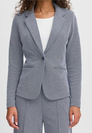 Persona que lleva una blazer gris entallada con un solo botón y pantalones a juego sobre una camiseta blanca con canalé.