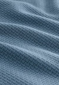 Tessuto blu testurizzato con un sottile motivo geometrico, presentato in morbide pieghe che evidenziano la sua trama intrecciata e la profondità del materiale.