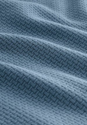 Texturerad blått tyg med ett subtilt geometriskt mönster, visad i mjuka veck som framhäver dess vävda textur och materialdjup.