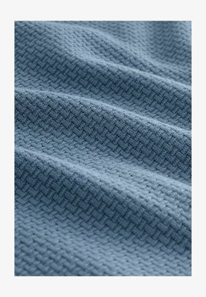 Textúrovaná modrá tkanina s jemným geometrickým vzorom, vystavená v mäkkých záhyboch, zdôrazňujúca svoju tkanú textúru a hĺbku materiálu.