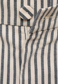 Gestreifter Stoff mit abwechselnd schmalen dunkelgrauen und off-white Streifen. Knopfverschluss mit einer glatten Textur in der Nähe der oberen Naht.