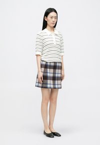 Strikket hvid polo med horisontale striber, parret med en ternet flared nederdel i brun, blå og beige. Sorte sko fuldender outfittet.