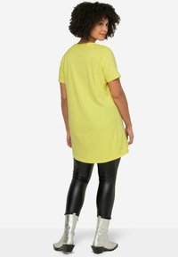 T-shirt giallo oversize con maniche corte, abbinato a leggings neri lucidi e stivali alla caviglia argentati con tacco a blocco.