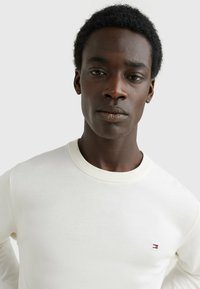 Maglione bianco in cotone con collo a girocollo a coste e maniche lunghe. Presenta un piccolo logo ricamato sul petto. Texture liscia.
